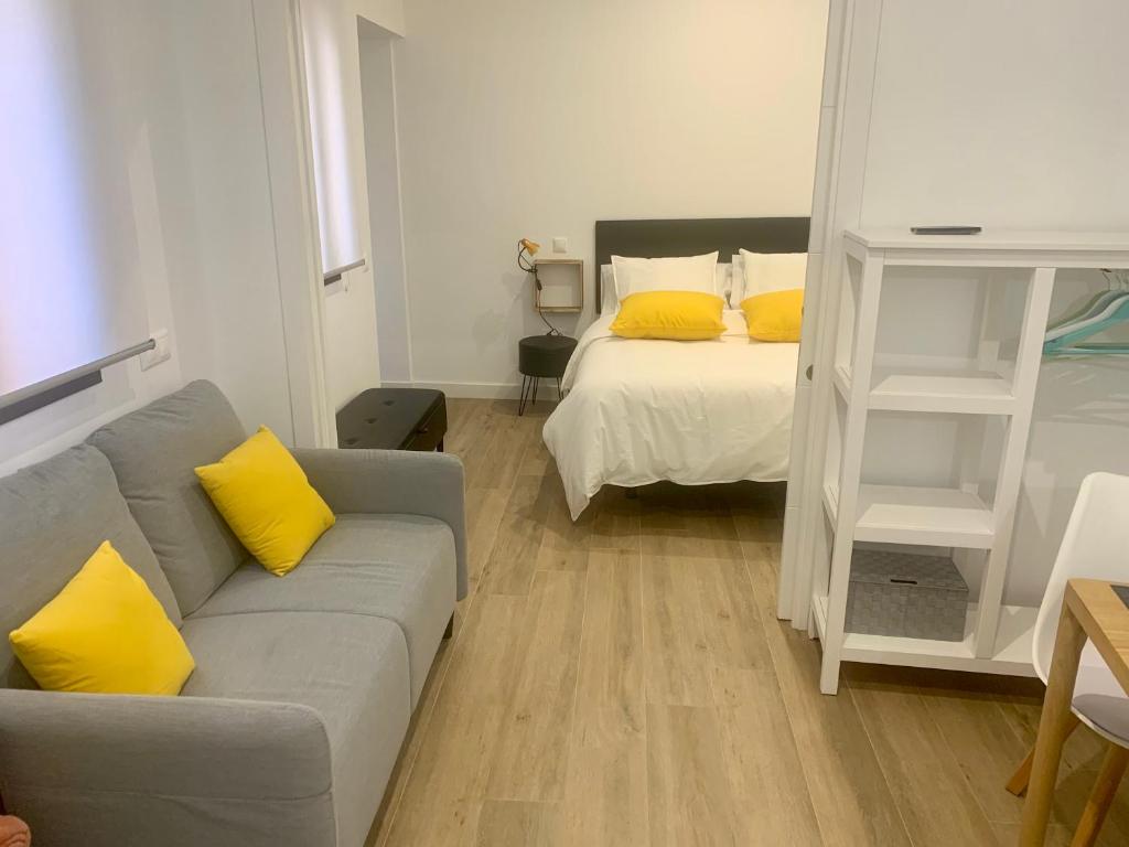 een woonkamer met een bank en een bed met gele kussens bij Puerta de Caceres Apartamento 5 Callejón De Don Álvaro in Cáceres