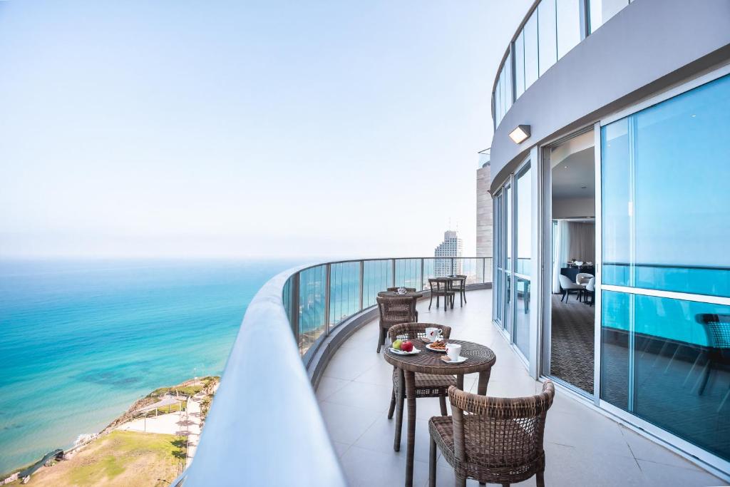 Ramada Hotel & Suites by Wyndham Netanya في نتانيا: شرفة مع طاولة وكراسي والمحيط