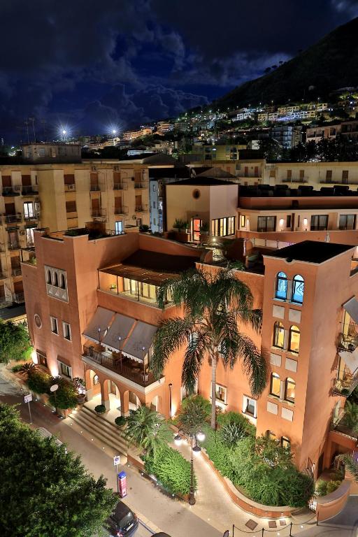 a large building with a palm tree in front of it at Artemis Hotel in Cefalù