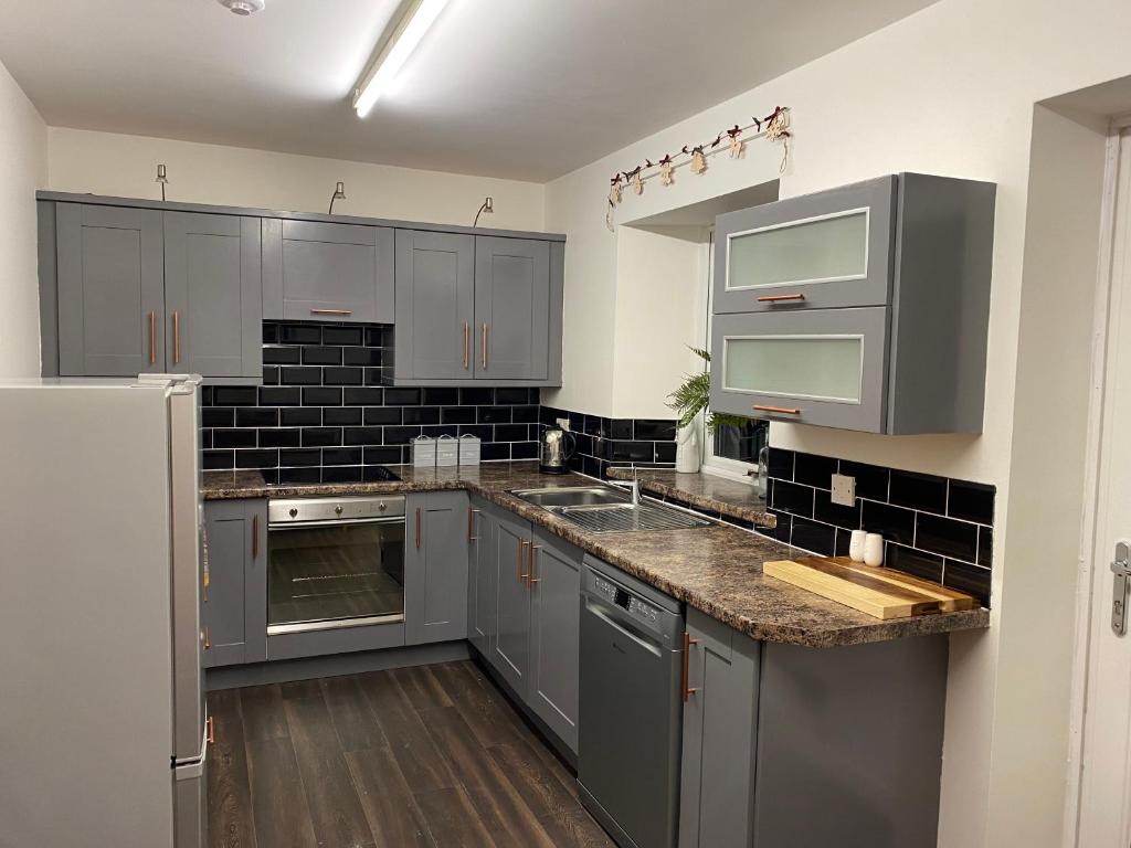 uma cozinha com armários cinzentos e electrodomésticos de aço inoxidável em Claire's Townhouse, Aberdeenshire, 3 bedrooms em Oldmeldrum