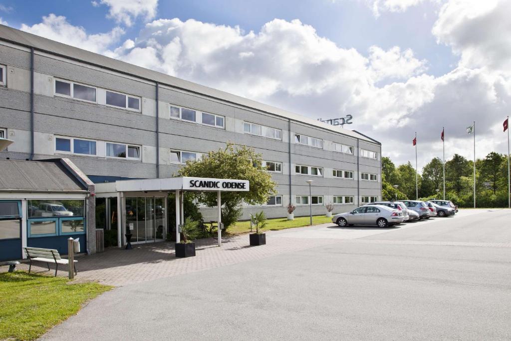 a large building with cars parked in a parking lot at Scandic Odense in Odense