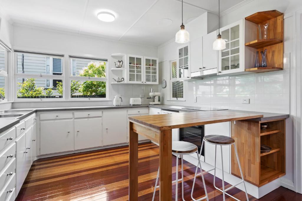 une cuisine avec des placards blancs et une table en bois dans l'établissement Artist's Cottage - Cosy Home in Quiet Leafy Street, à Toowoomba