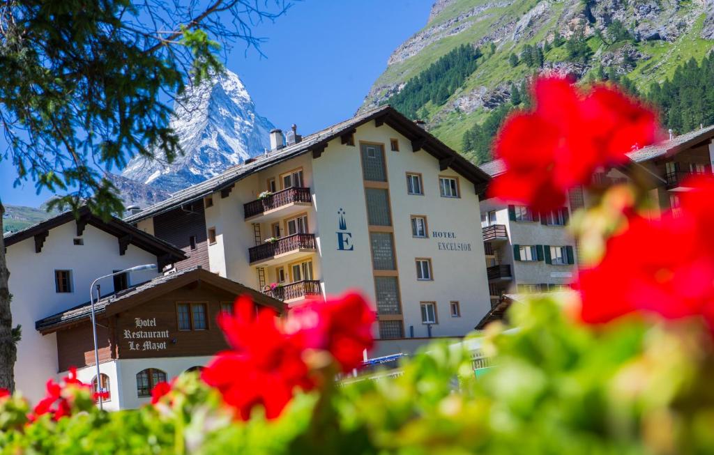 a hotel in front of a mountain with red flowers at Hotel Excelsior in Zermatt