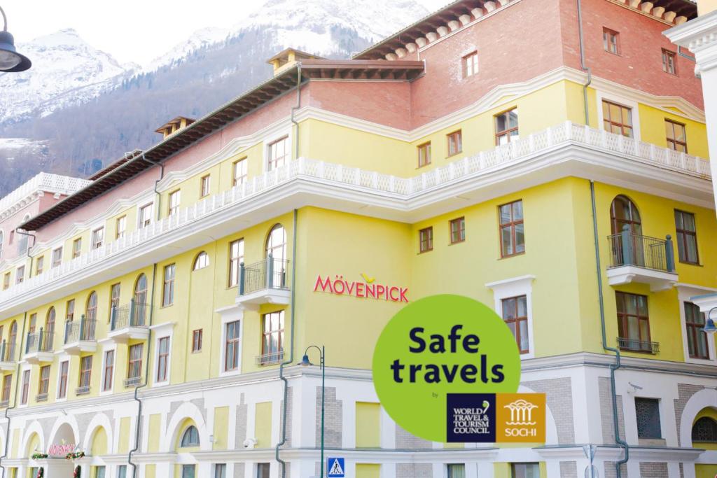 a yellow building with a sign that reads safe travels at Mövenpick Hotel Krasnaya Polyana in Estosadok