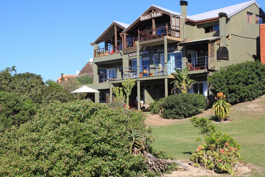 a large house on top of a hill with bushes at Beach Music in Jeffreys Bay