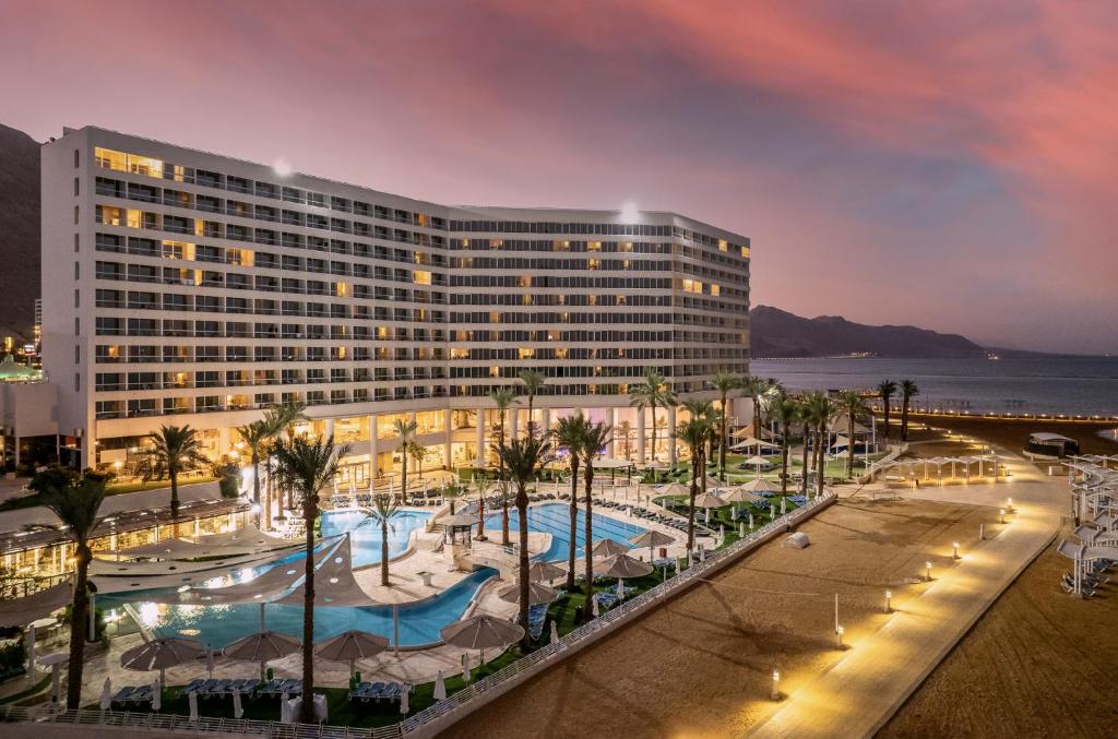 a hotel with a pool and palm trees in front of a building at Vert Dead Sea by AFI Hotels in Ein Bokek