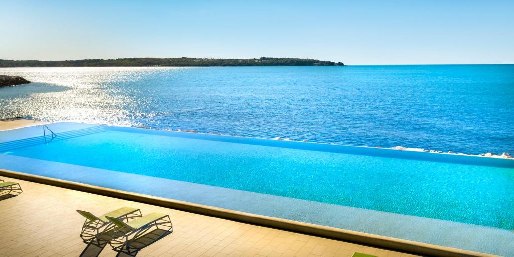a swimming pool with two chairs and the water at Aminess Vival Maestral Hotel in Novigrad Istria
