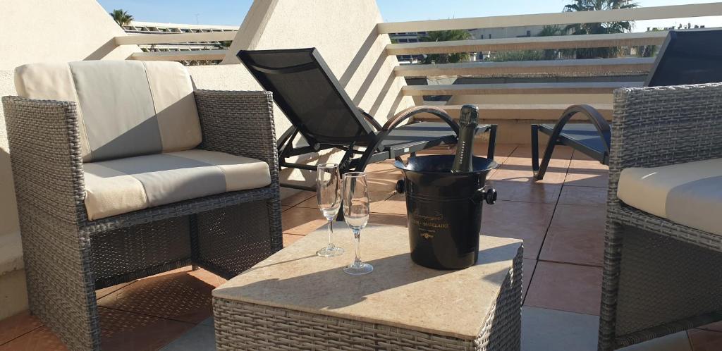 a patio with two chairs and a trash can with wine glasses at Studio Naturiste CAPTIVE Héliopolis FG 13 in Cap d'Agde