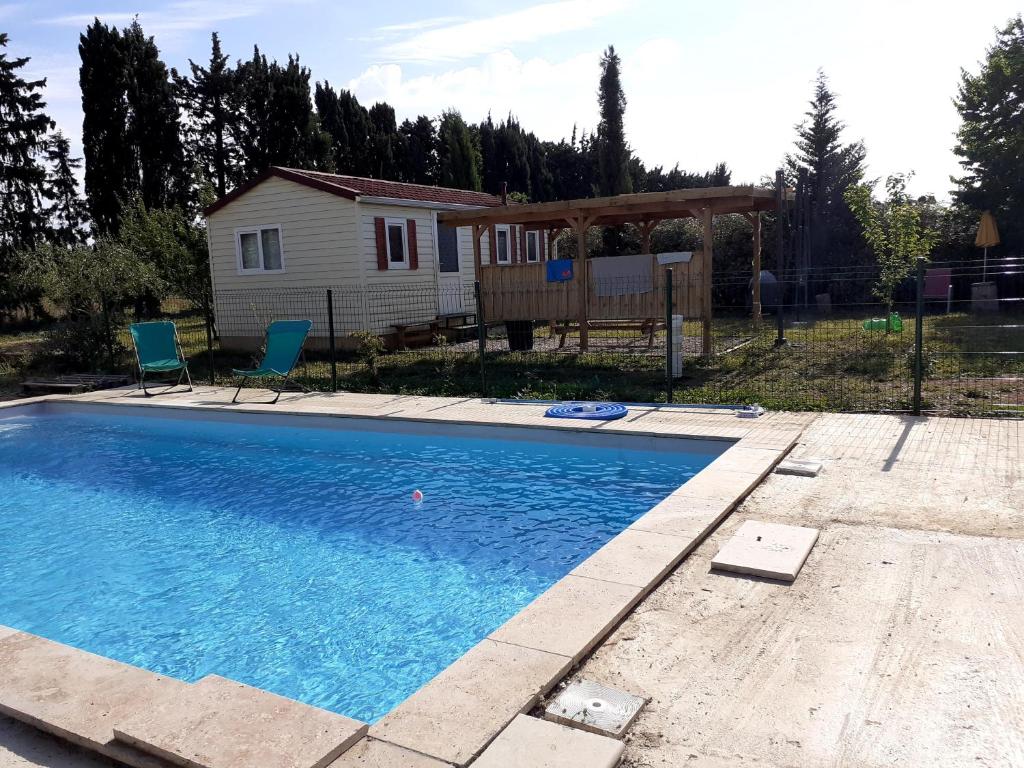 une piscine avec deux chaises et une maison dans l'établissement Mobilhome & Piscine - Sud-Alpilles - Oliveraie bio, à Entressen