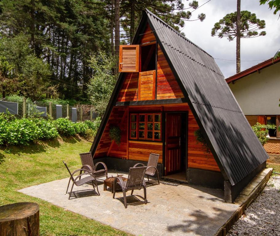 a small house with a black roof and chairs at Empório reserva da serra - Opções de chalés e Hidromassagem in Campos do Jordão