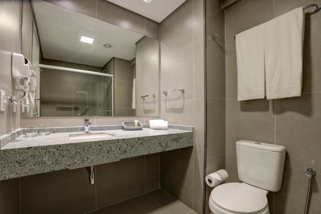 a bathroom with a toilet and a sink and a mirror at Comfort Hotel Guarulhos Aeroporto in Guarulhos