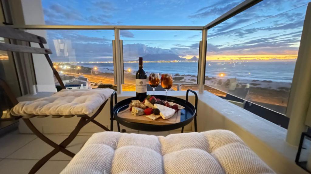 a balcony with a table with a bottle of wine and a glass at Abode Africa in Bloubergstrand