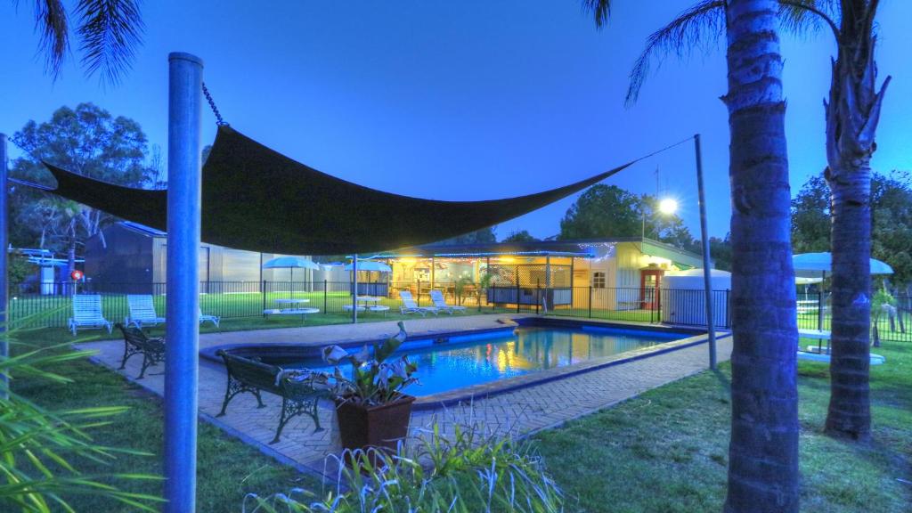 a swimming pool with a hammock next to a house at River Bend Caravan Park in Kanyapella