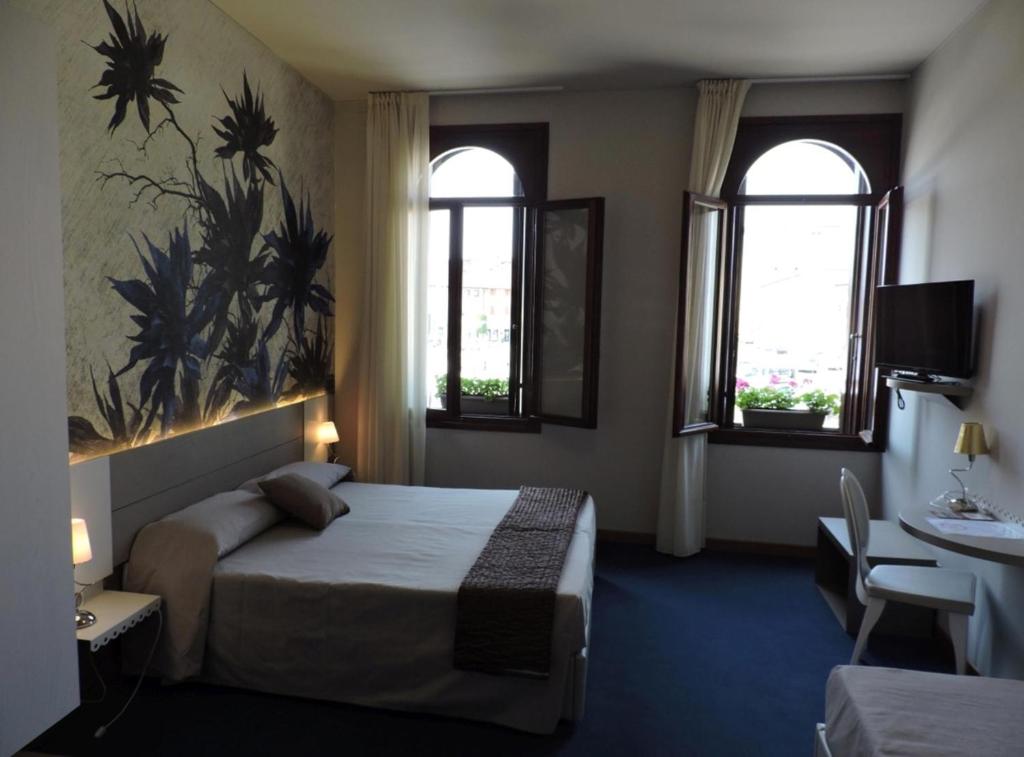 a hotel room with a bed and two windows at Albergo Leon D'Oro in Maniago