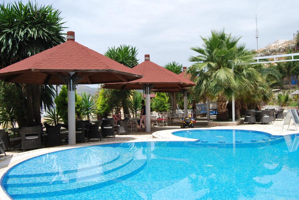 a swimming pool with an umbrella and palm trees at Hotel Panorama Sarande in Sarandë