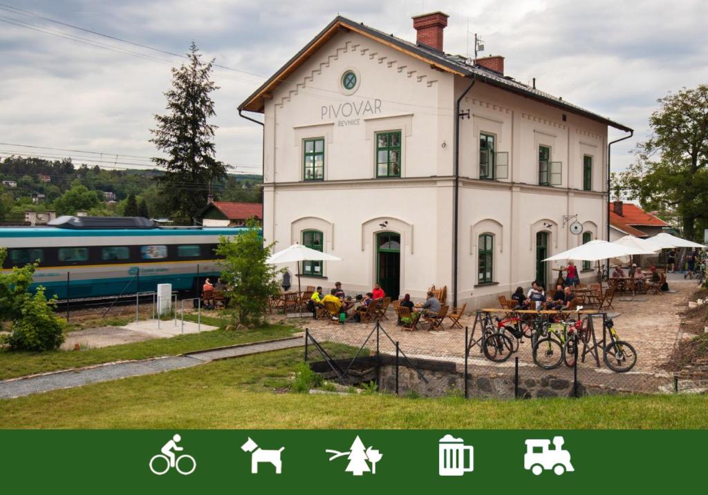 a building with people sitting at tables in front of a train at Pivovar Řevnice in Řevnice