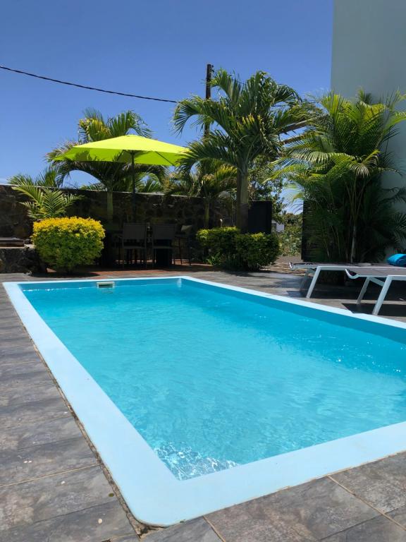a swimming pool with blue water and an umbrella at Villa Prana île Maurice in Grand-Baie