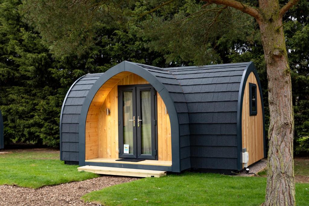 a small house with a black roof and a tree at Camping Pods Trevella Holiday Park in Crantock