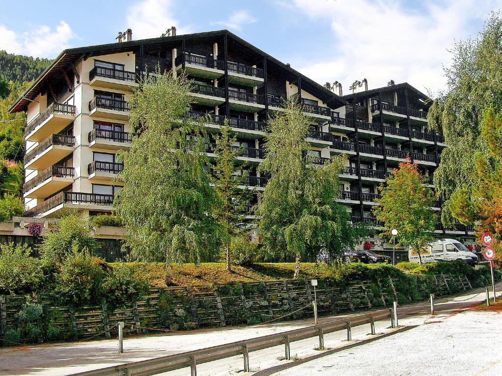un grand immeuble d'appartements avec des arbres devant lui dans l'établissement Apartment Eden Roc 28 by Interhome, à Nendaz