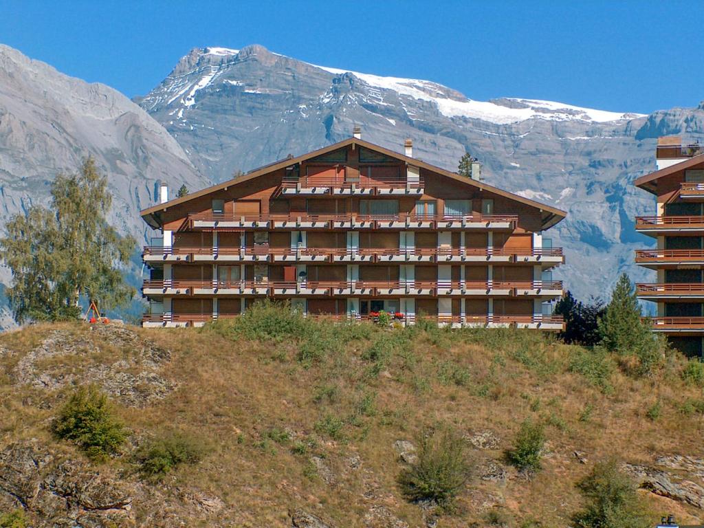 ein großes Gebäude auf einem Hügel mit einem Berg in der Unterkunft Apartment Rossignol C4 by Interhome in Nendaz