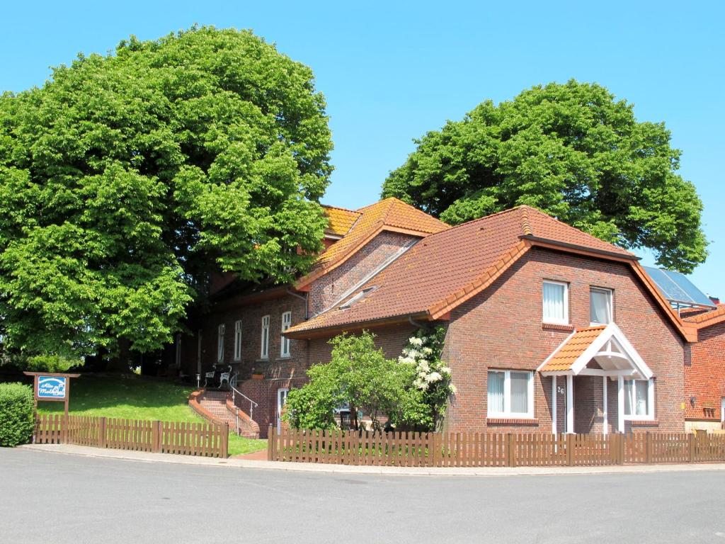 a brown brick house with a fence and trees at Apartment Alte Molkerei-1 by Interhome in Friederikensiel