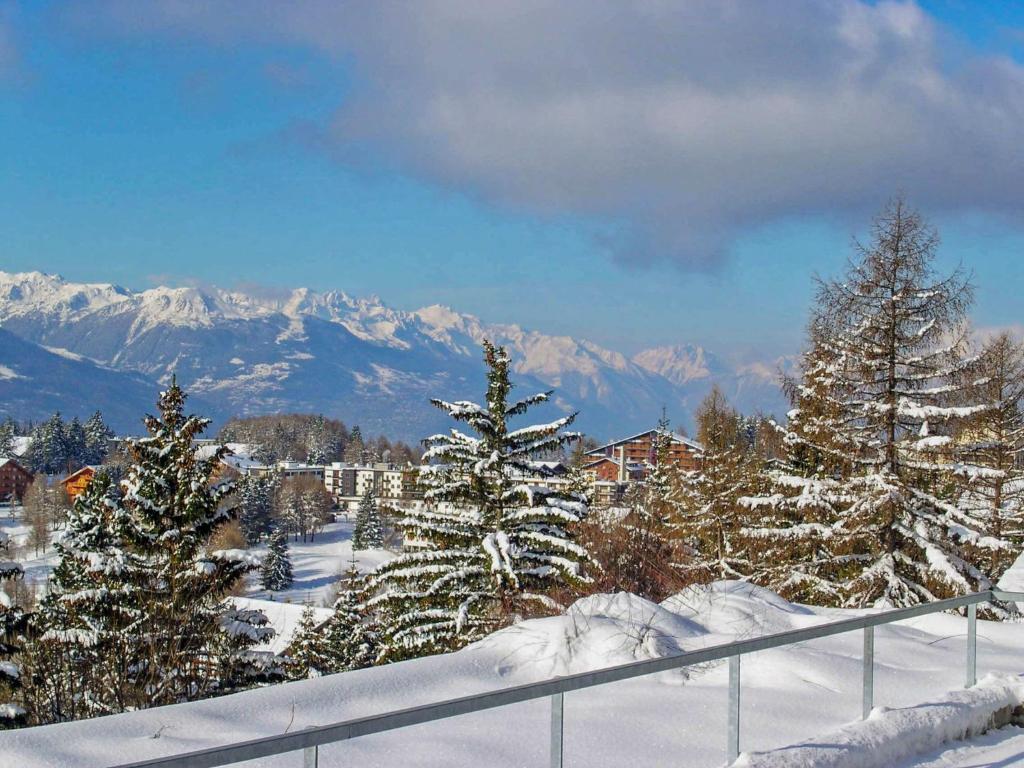 a group of trees covered in snow with mountains in the background at Apartment Jeanne D'Arc Apt- C-19 by Interhome in Crans-Montana