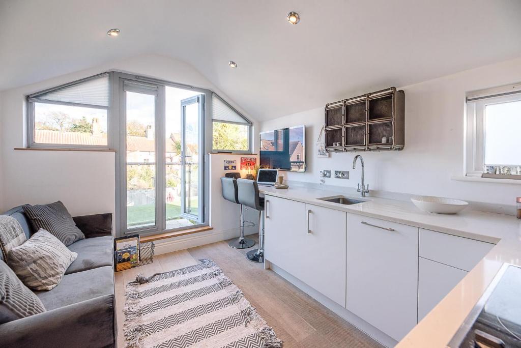 a kitchen with white cabinets and a couch at Papillon Southwold - A Modern Flat with Balcony in Southwold