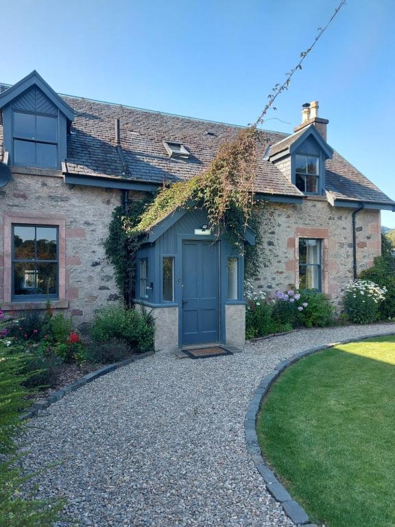 una casa con una puerta azul en una entrada de grava en The Cottage, The Loch Ness Cottage Collection, en Inverness