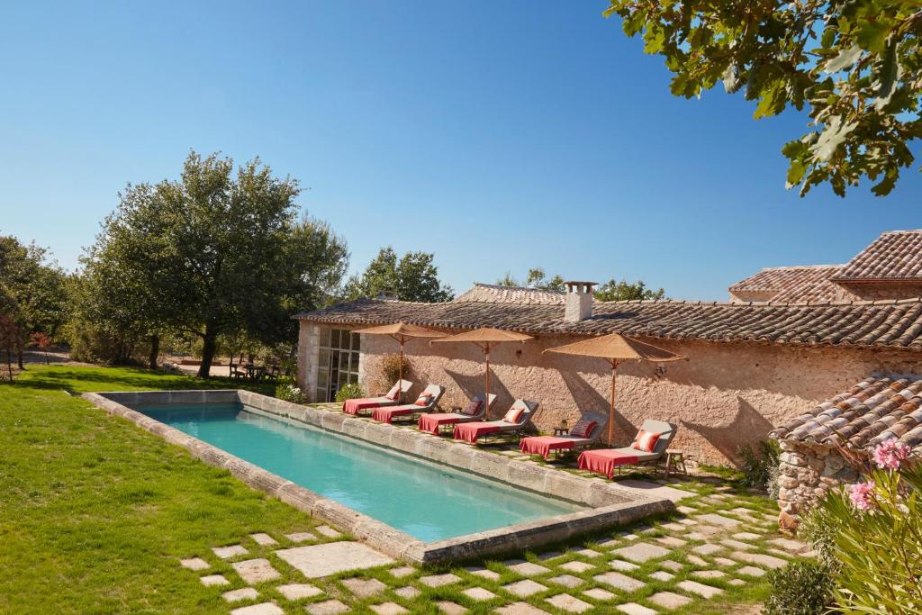 a pool with chairs and umbrellas next to a house at Le Mas Vermentino, La Bastide de Marie, Villa avec services in Ménerbes