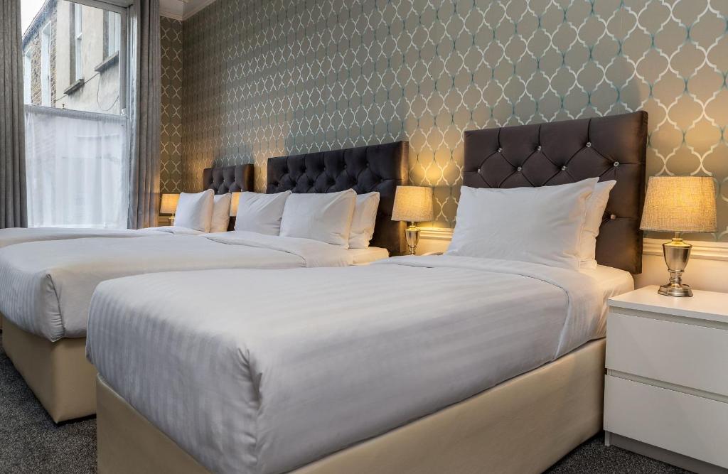 duas camas num quarto de hotel com almofadas brancas em Clifden House by Nina em Dublin
