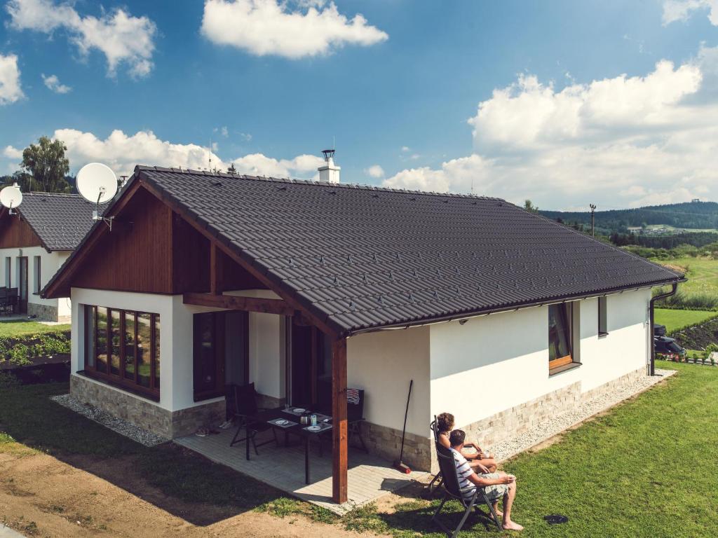 dos personas sentadas fuera de una casa pequeña en Holiday Home Residence Lipno by Interhome, en Lipno nad Vltavou