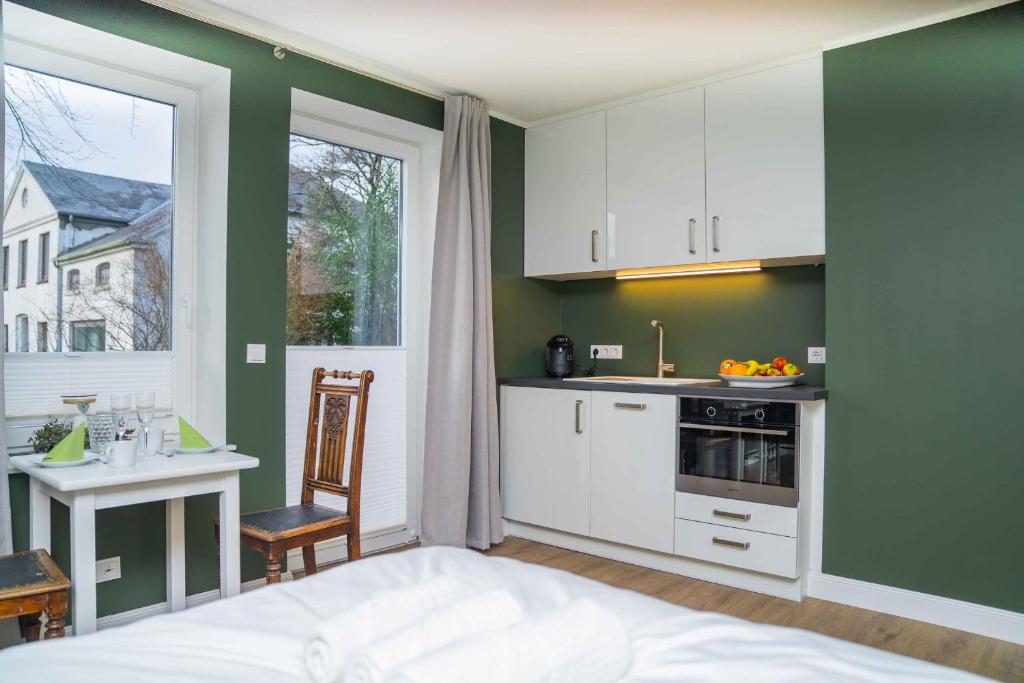une cuisine avec des murs verts, des armoires blanches et une table dans l'établissement Gästehaus "Alte Bücherei" Satrup - a50559, à Mittelangeln
