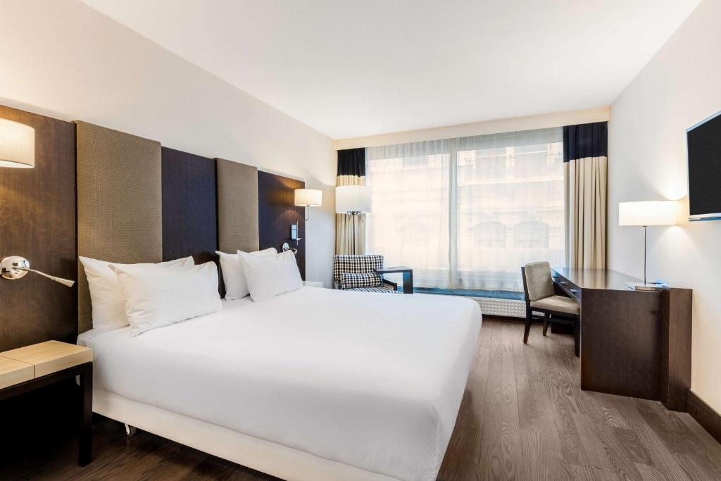Cette chambre comprend un grand lit blanc et un bureau. dans l'établissement NH Hotel Stephanie, à Bruxelles