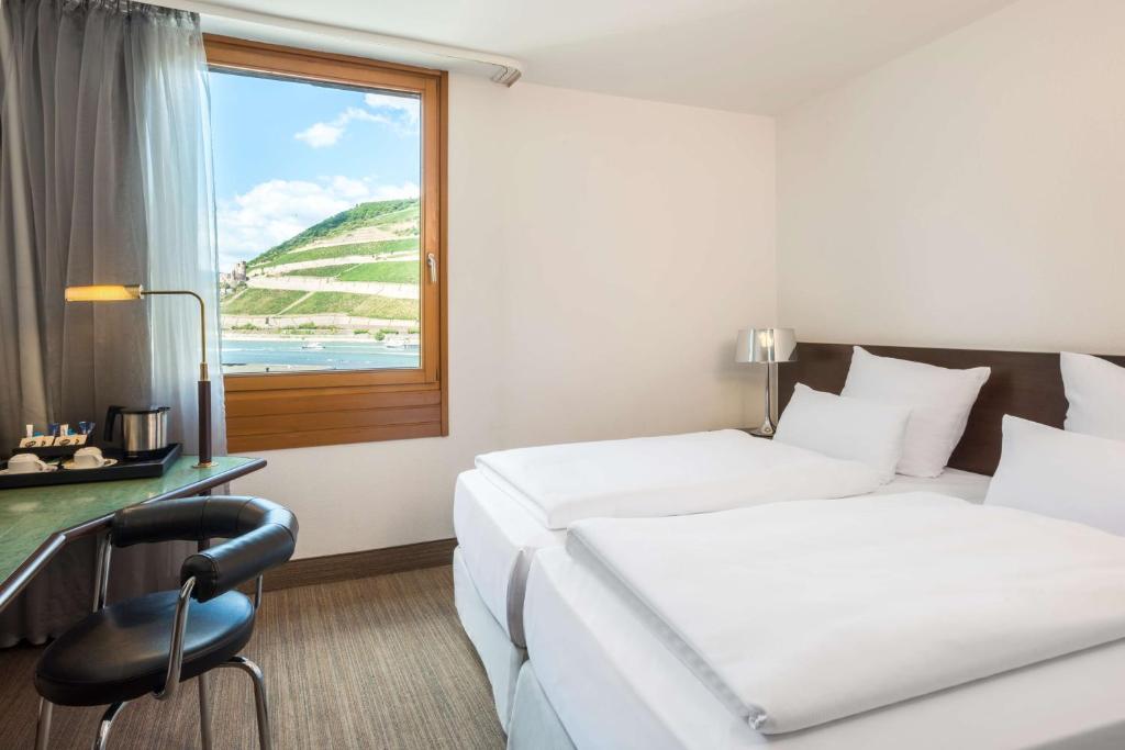 a hotel room with two beds and a desk and a window at NH Bingen in Bingen am Rhein