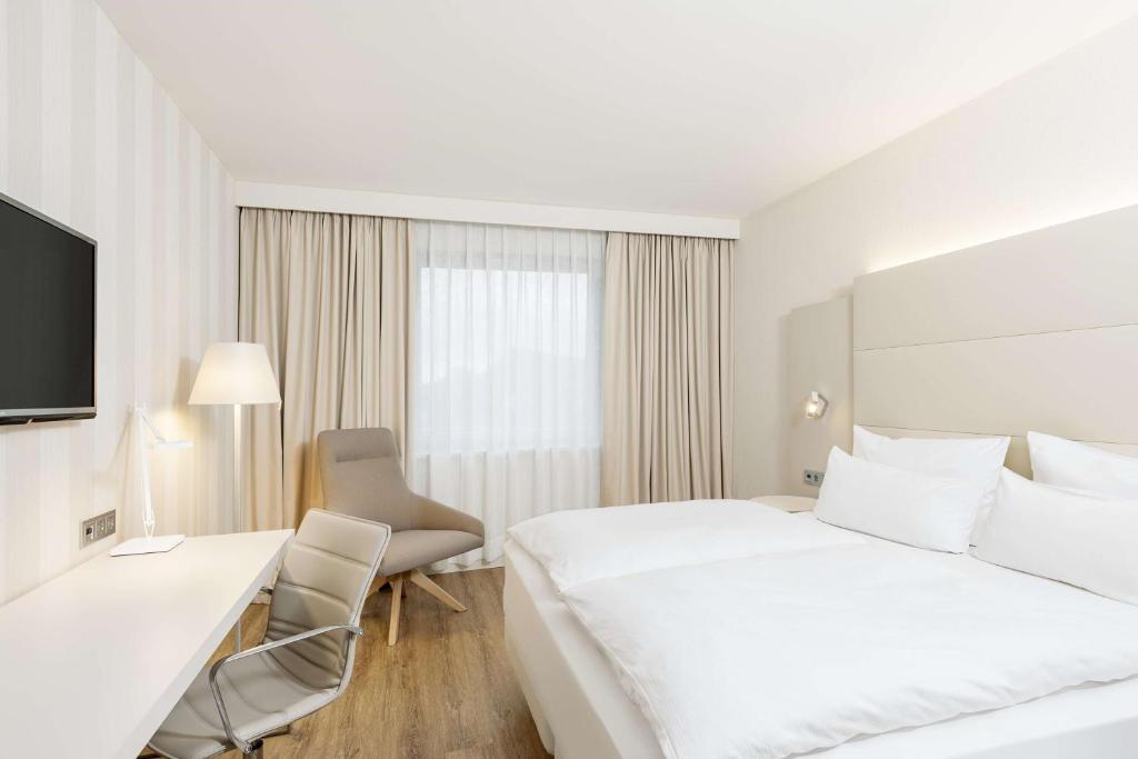 ein Hotelzimmer mit einem großen weißen Bett und einem Schreibtisch in der Unterkunft NH Düsseldorf City Nord in Düsseldorf