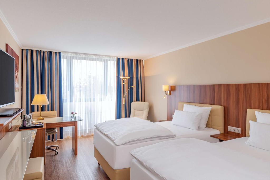 a hotel room with two beds and a desk and a television at NH Ingolstadt in Ingolstadt