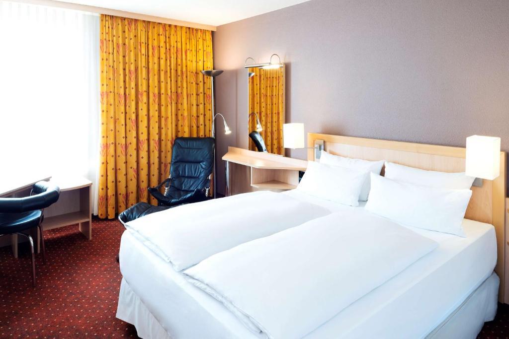 a hotel room with a large white bed and a desk at NH Leipzig Messe in Leipzig