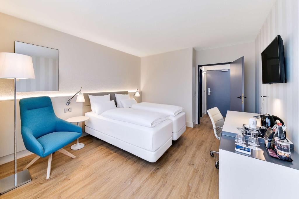 a hotel room with a white bed and a blue chair at NH Weinheim in Weinheim