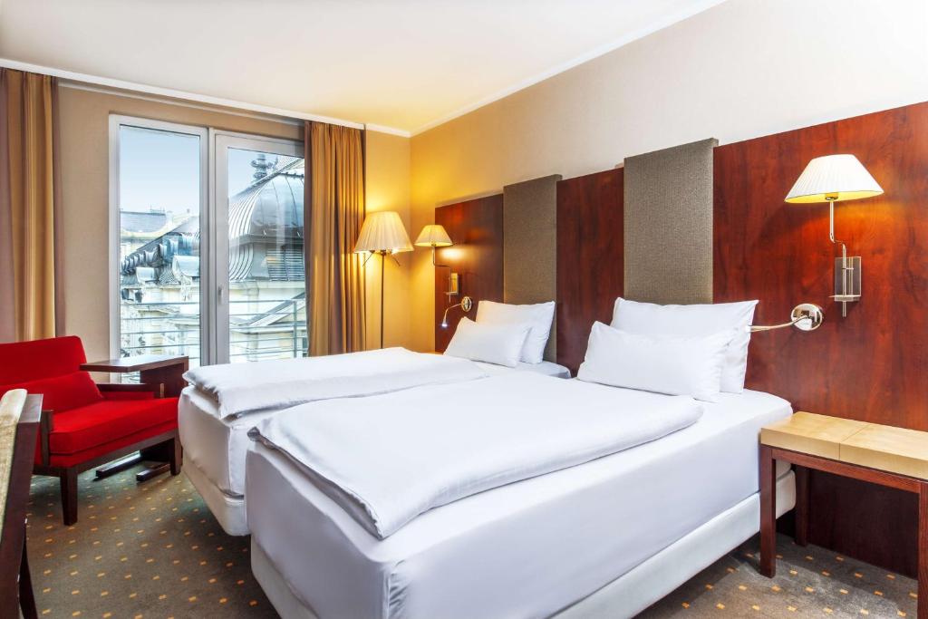 a hotel room with two beds and a red chair at NH Budapest City in Budapest