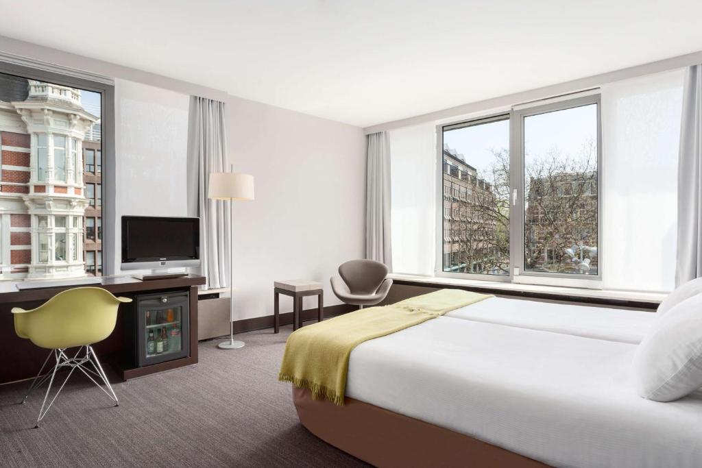 a hotel room with a bed and a large window at NH Amsterdam Caransa in Amsterdam