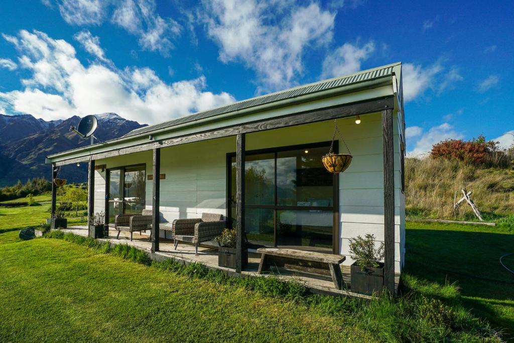 ein Haus mit Glastüren und einer Bank auf einem Feld in der Unterkunft Glendhu Station Cottage - Glendhu Bay Holiday Home in Glendhu