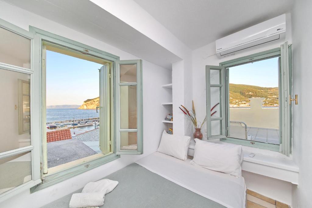 een witte kamer met ramen en een witte bank bij Faros Coastal Apartments in Skopelos Town