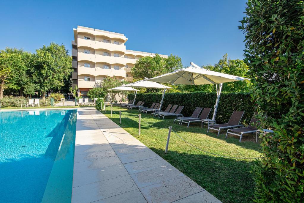 einen Pool mit Stühlen und Sonnenschirmen neben einem Gebäude in der Unterkunft Hotel La Pergola Dependance in Lignano Sabbiadoro