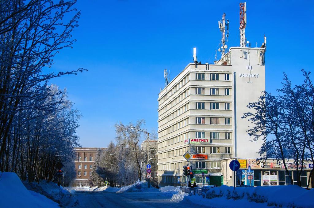 a tall white building on a snowy city street at Ametist Hotel in Apatity