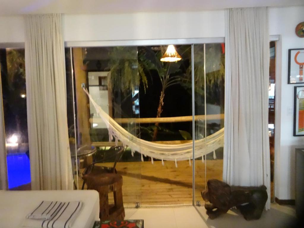 a living room with a large window with a hammock at Bangalô no alto da colina no Villas do Pratagy - Maceió in Maceió