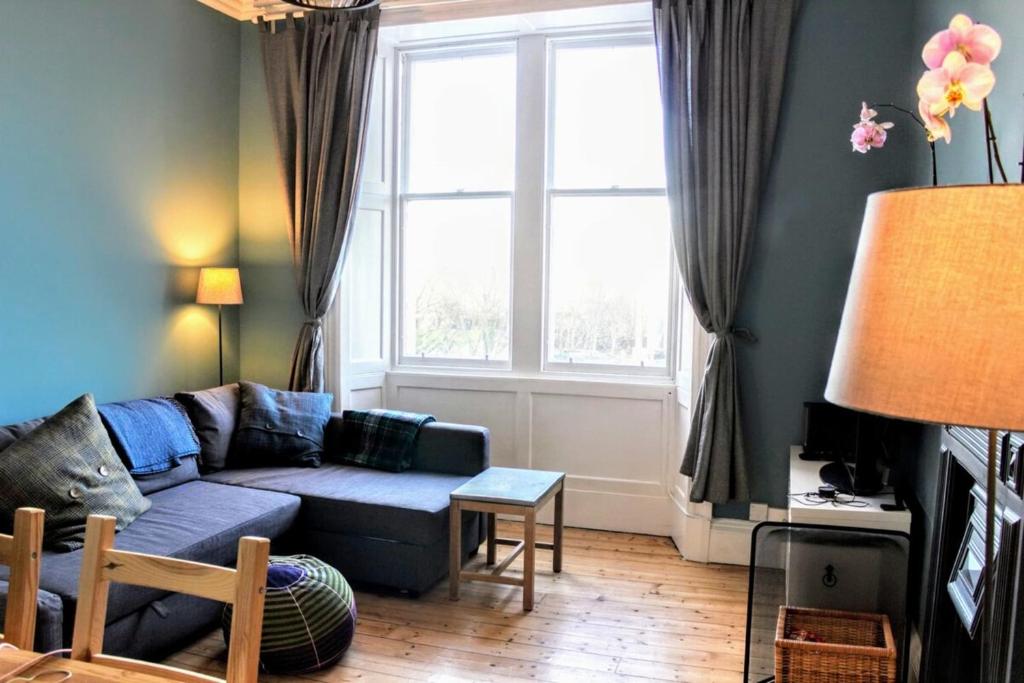 ein Wohnzimmer mit einem blauen Sofa und einem Fenster in der Unterkunft Bright Modern Arthurs Seat 2 Bedroom Apartment in Edinburgh