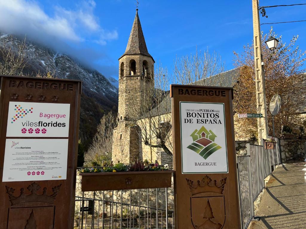 dois sinais em frente a uma igreja com uma torre em Casa de piedra con encanto en el bonito pueblo de Bagergue em Bagergue