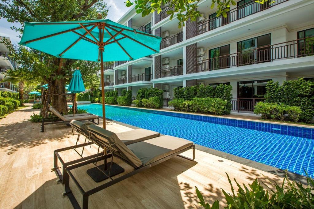 a hotel with a swimming pool and a blue umbrella and chairs at The Title Condo by Tropiclook in Rawai Beach