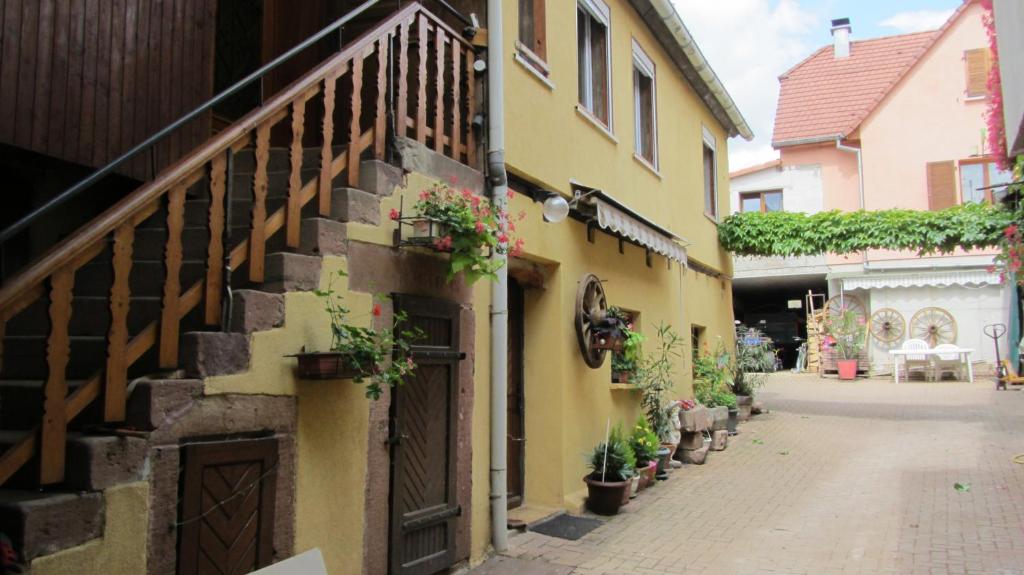 an alley with a yellow building with potted plants at Gîte du Vignoble in Beblenheim