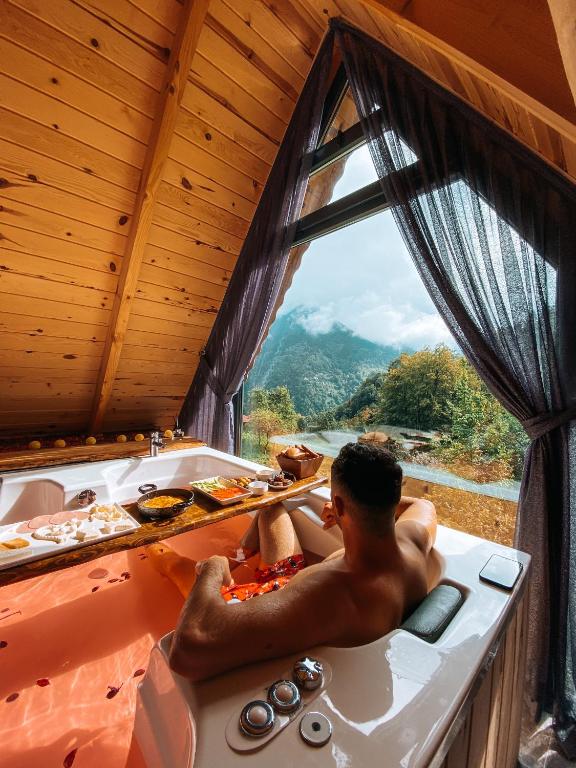 a man sitting in a bath tub with a window at Riona dağ evleri in Çamlıhemşin
